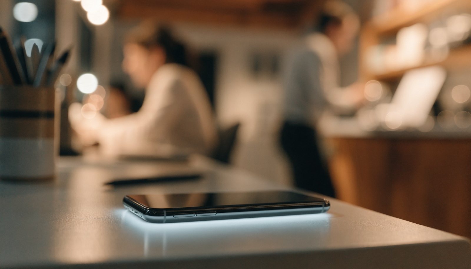 A sleek smartphone glowing softly on a clean desk inside a busy small business